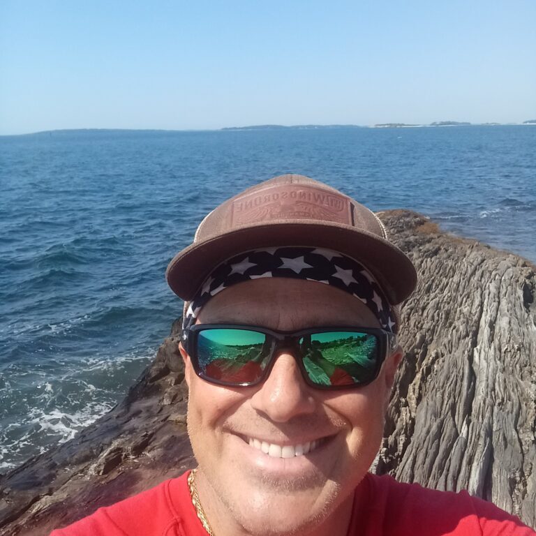 Man smiling by the ocean on a rock.