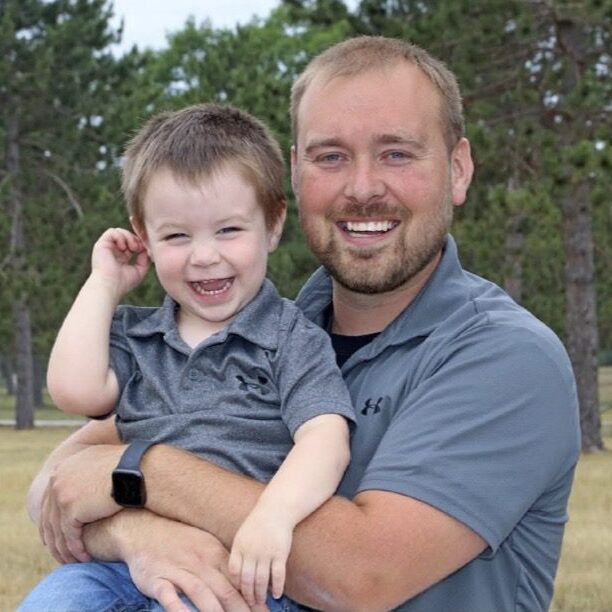 Smiling man holding a happy child outdoors.