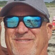 Man wearing sunglasses and cap at beach.