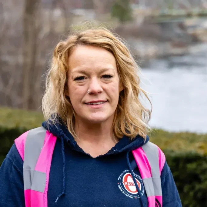 Smiling woman in a reflective vest outdoors.