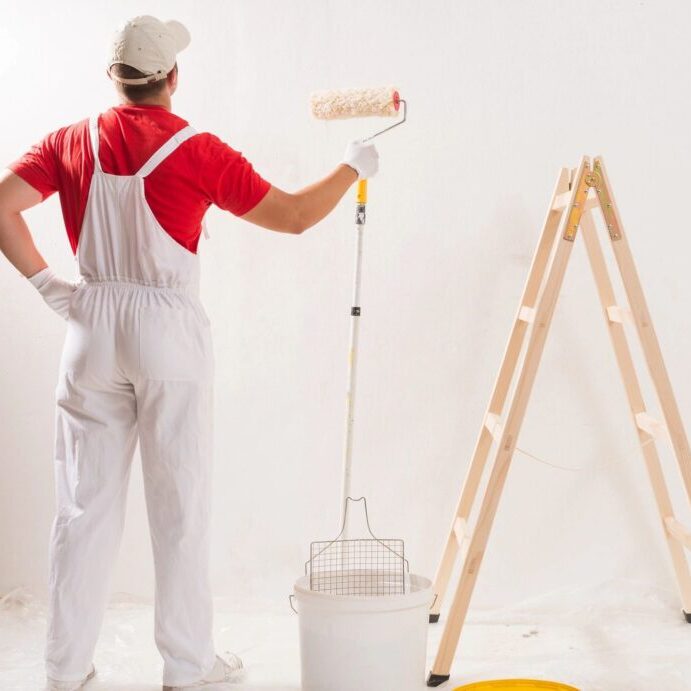Painter in overalls painting a white wall.